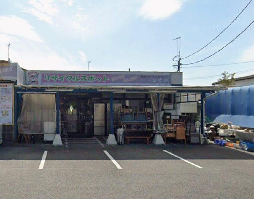「リサイクルショップアイスタ 湯河原店」の店舗外観。ピンク色の大きな看板に「リサイクルスポット」「買取ります 買います」と書かれ、店頭の駐車スペースや、並べられた中古家電、家具、雑貨が見える。